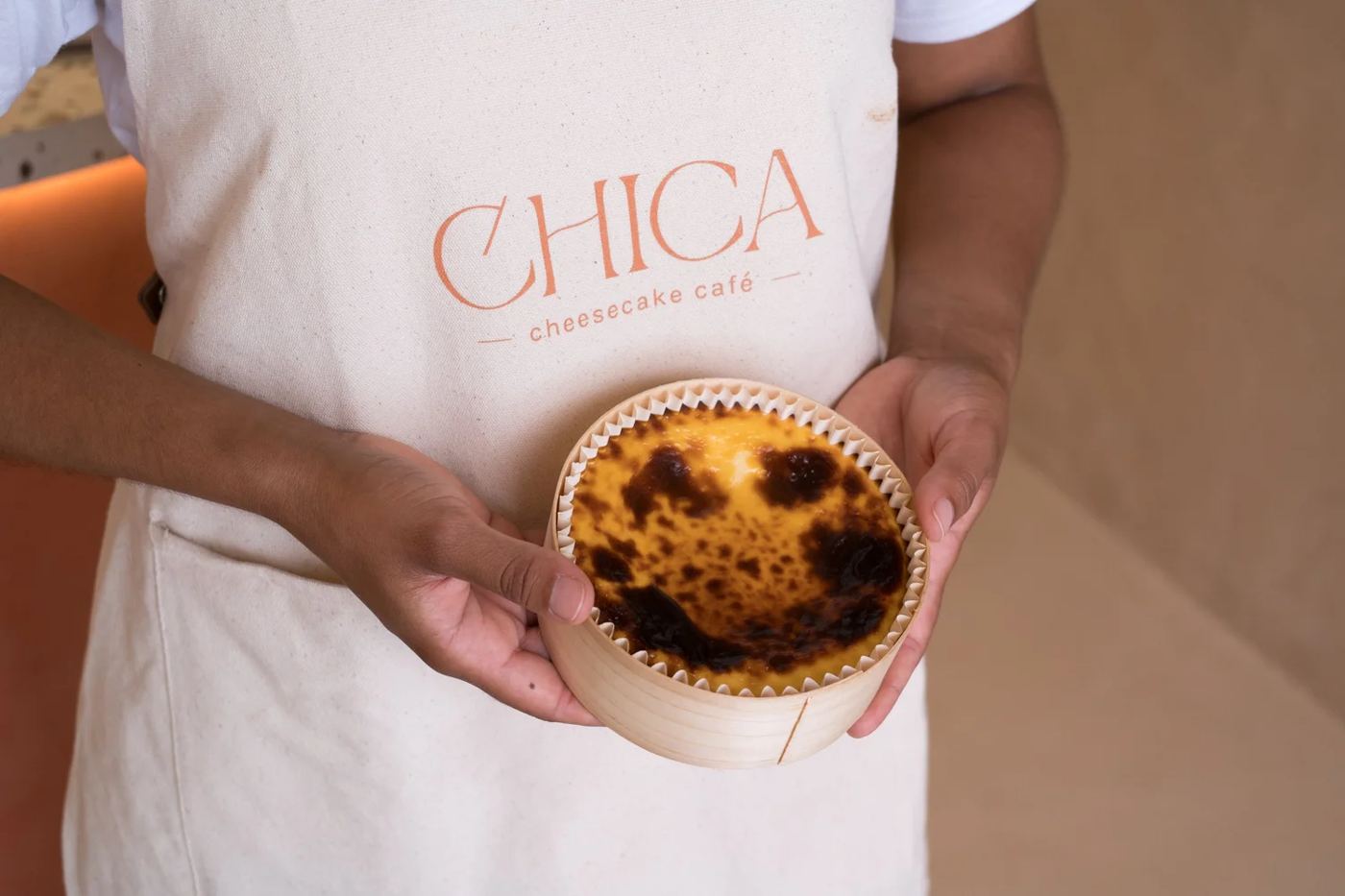 Una cheesecake de CHICA en su caja de madera, sostenida con el delantal de CHICA